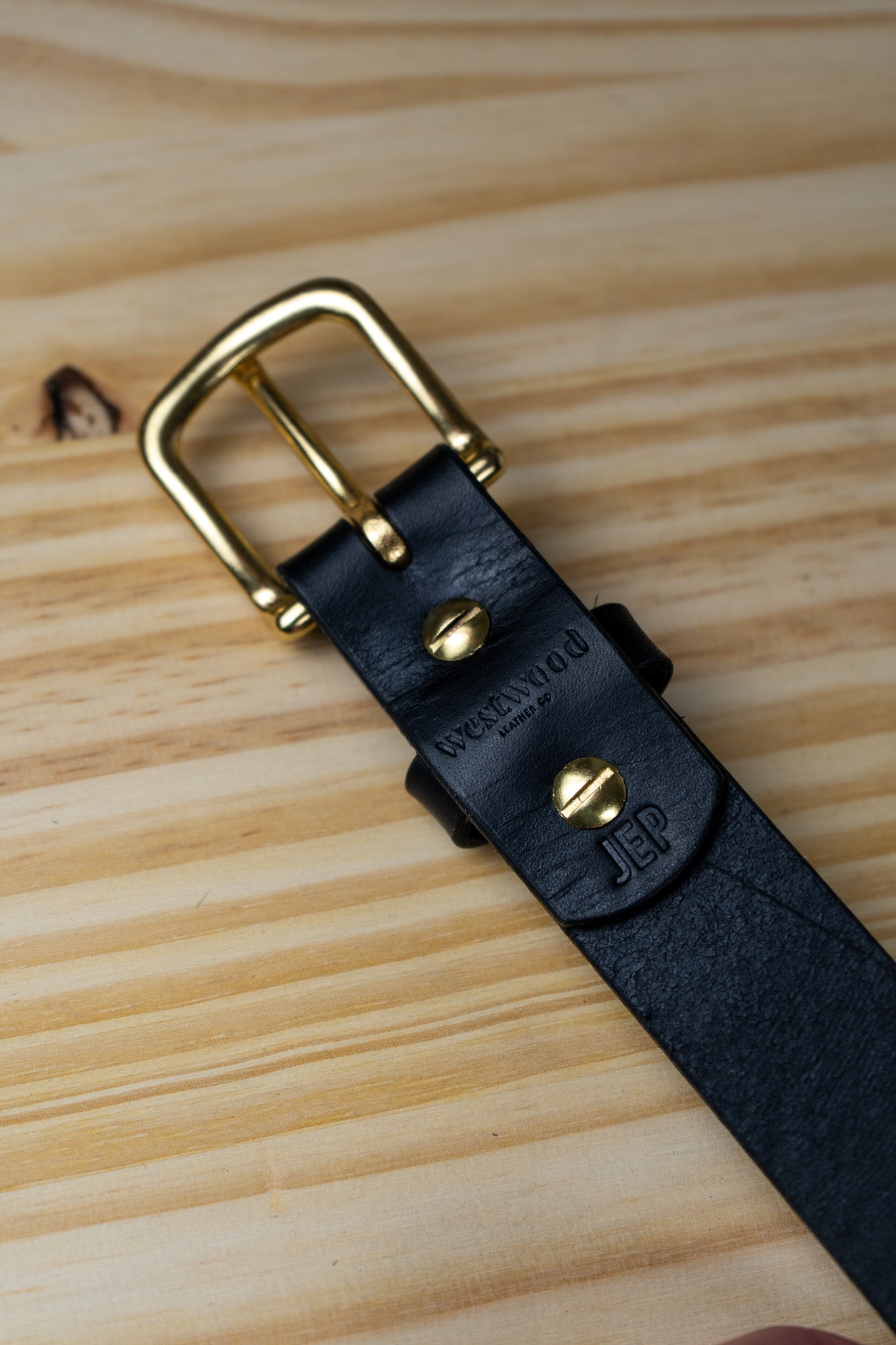 Black leather belt with gold buckle on a wooden surface