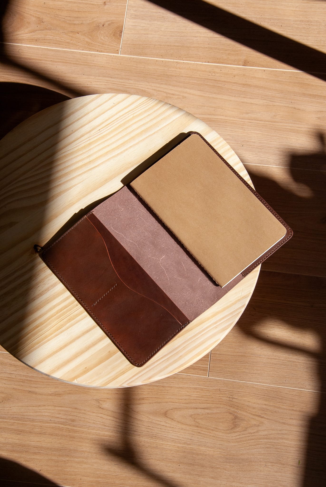 Brown leather journal cover on a wooden surface with sunlight casting shadows.