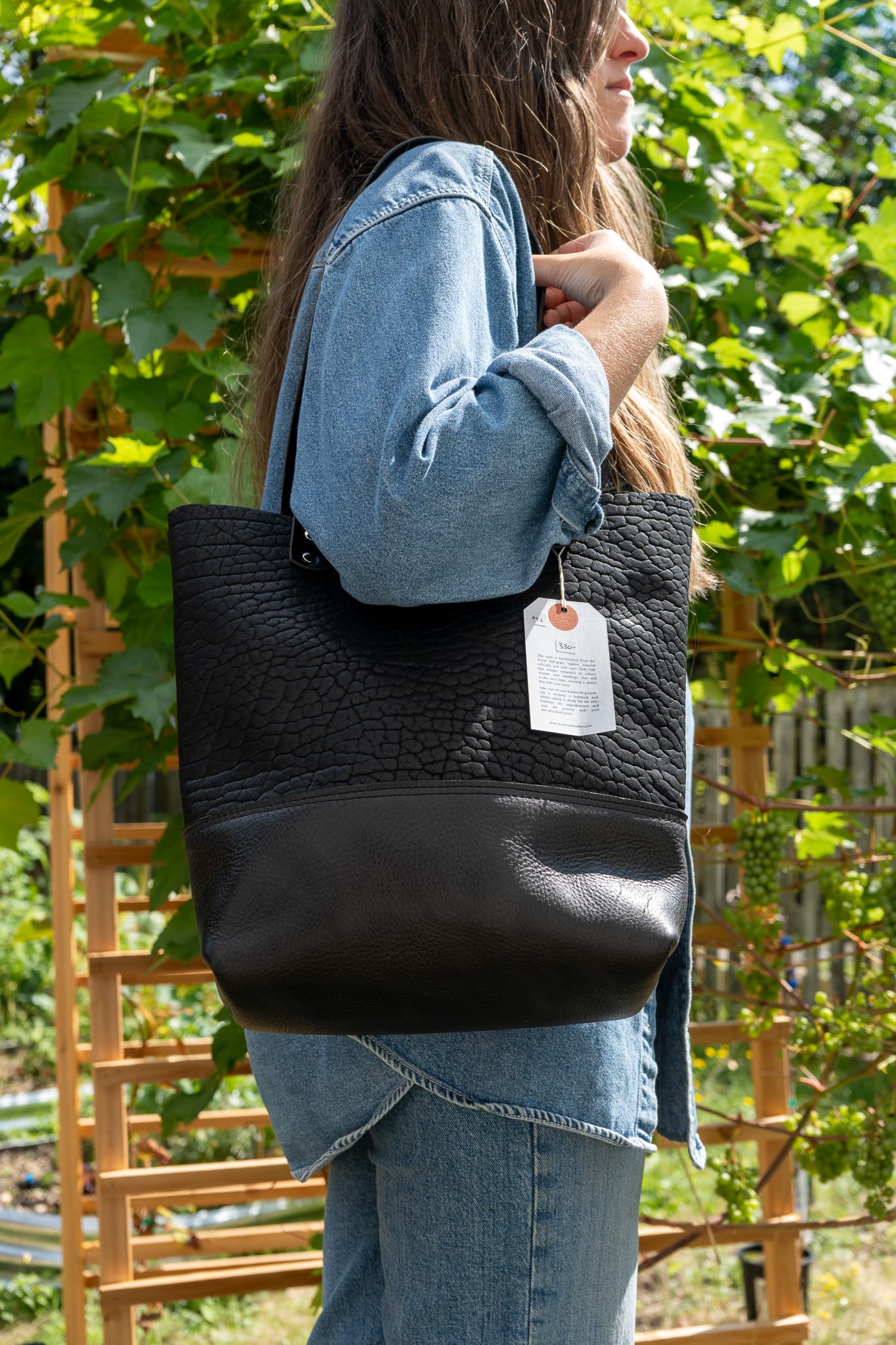 Person wearing a black woven tote bag with a visible brand tag outdoors.