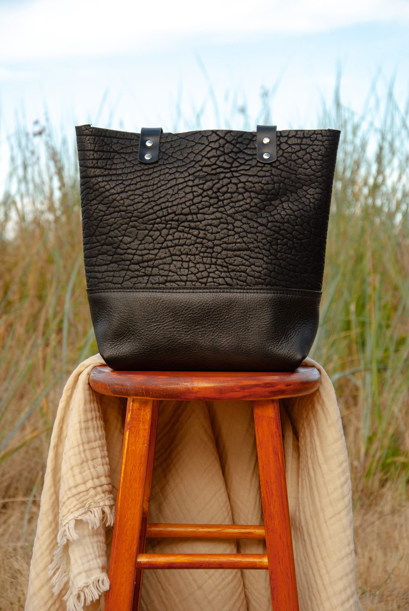 Black textured tote bag on a wooden stool with a natural background