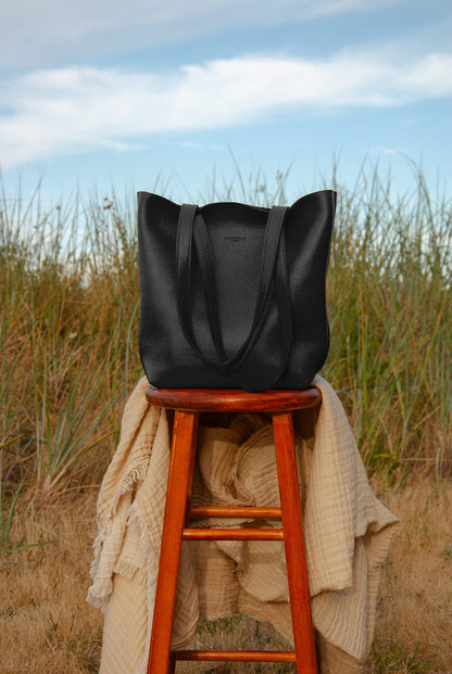 Black tote bag on a wooden stool with grass and blue sky in the background