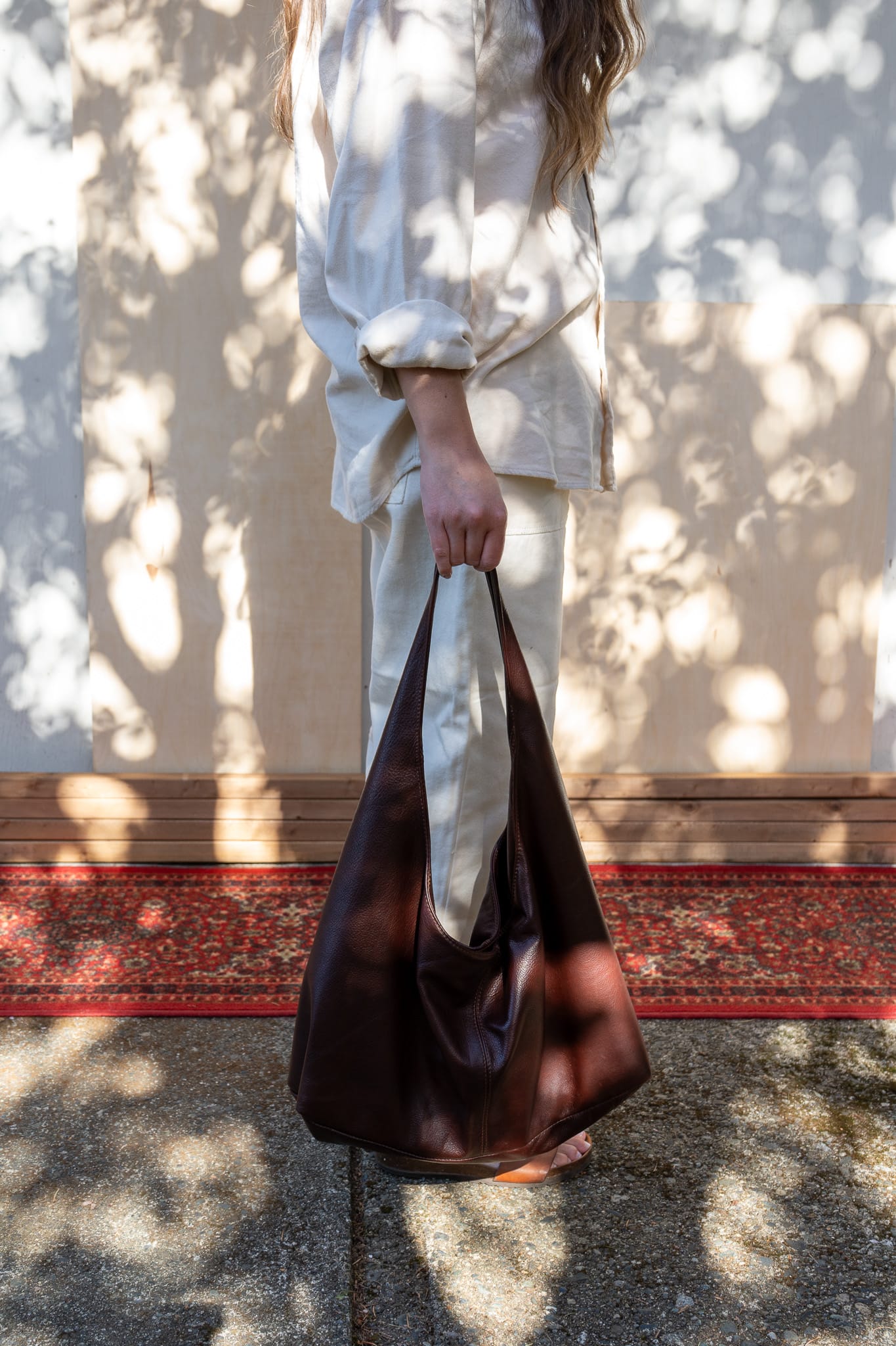 a person in a white shirt and pants is seen from the side, carrying a brown tote bag above the ground.