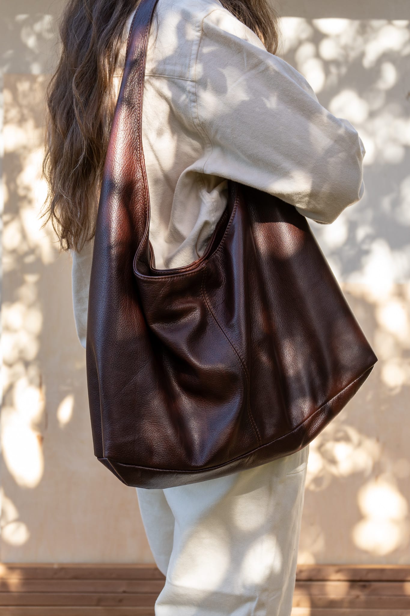 A person wearing a white shirt is seen from the back, carrying a large brown tote bag over their shoulder.