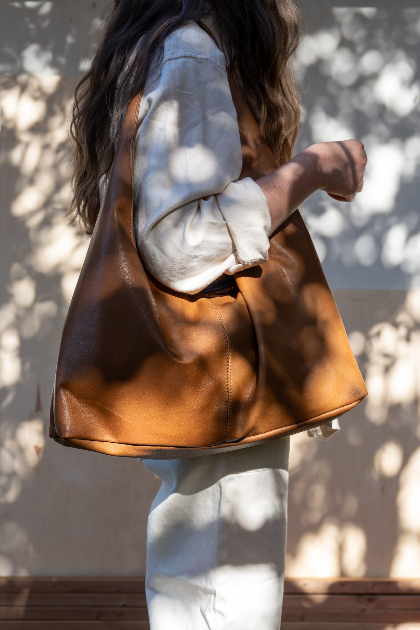 A person wearing a white shirt is seen from the side, carrying a large brown tote bag over their shoulder.