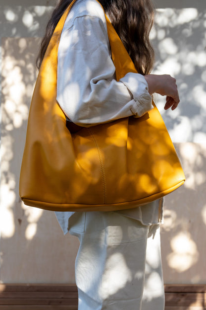 A person wearing a white shirt is seen from the side, carrying a large yellow tote bag over their shoulder.