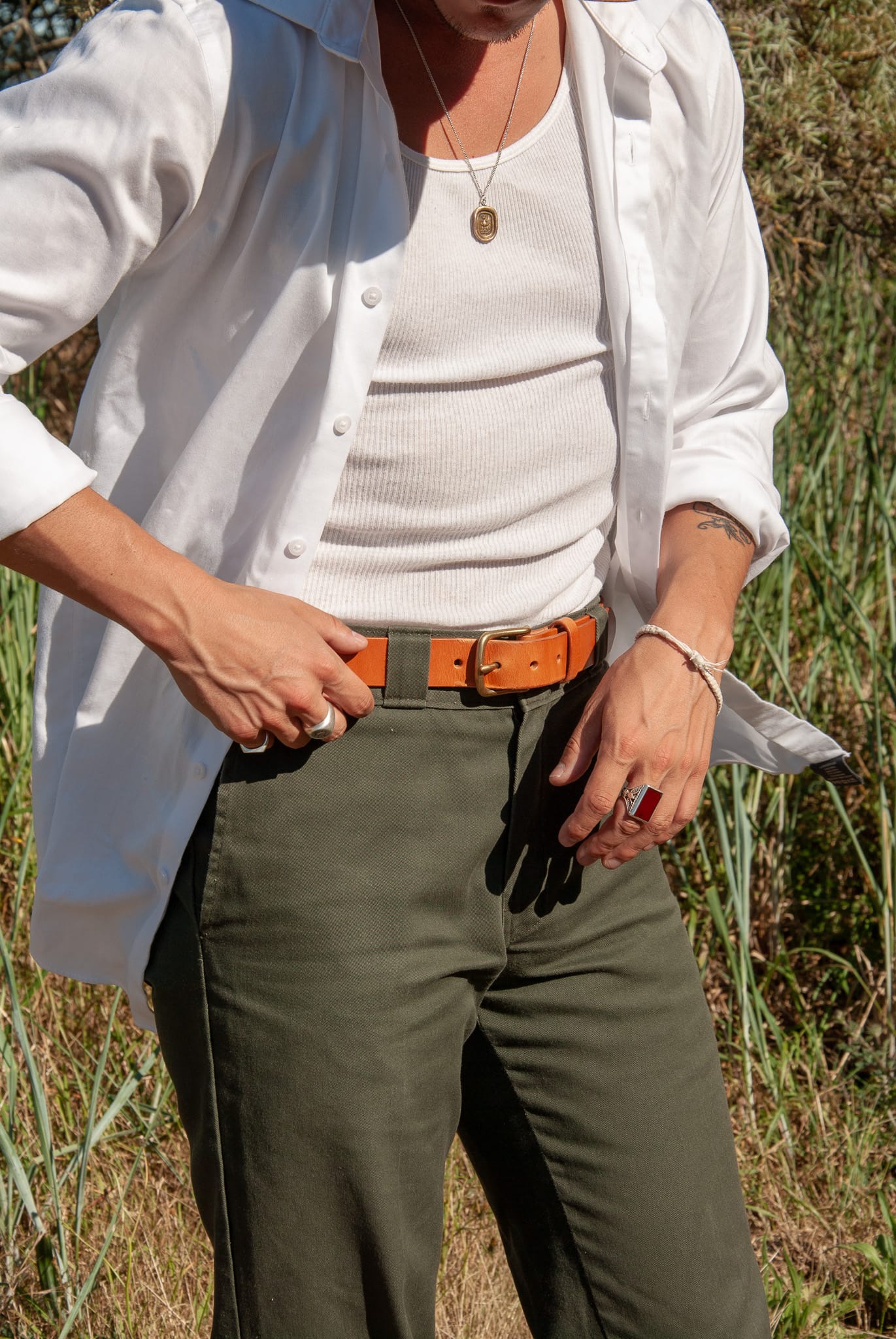 Person wearing a white shirt, white vest, green pants, and an orange belt in a grassy outdoor setting.