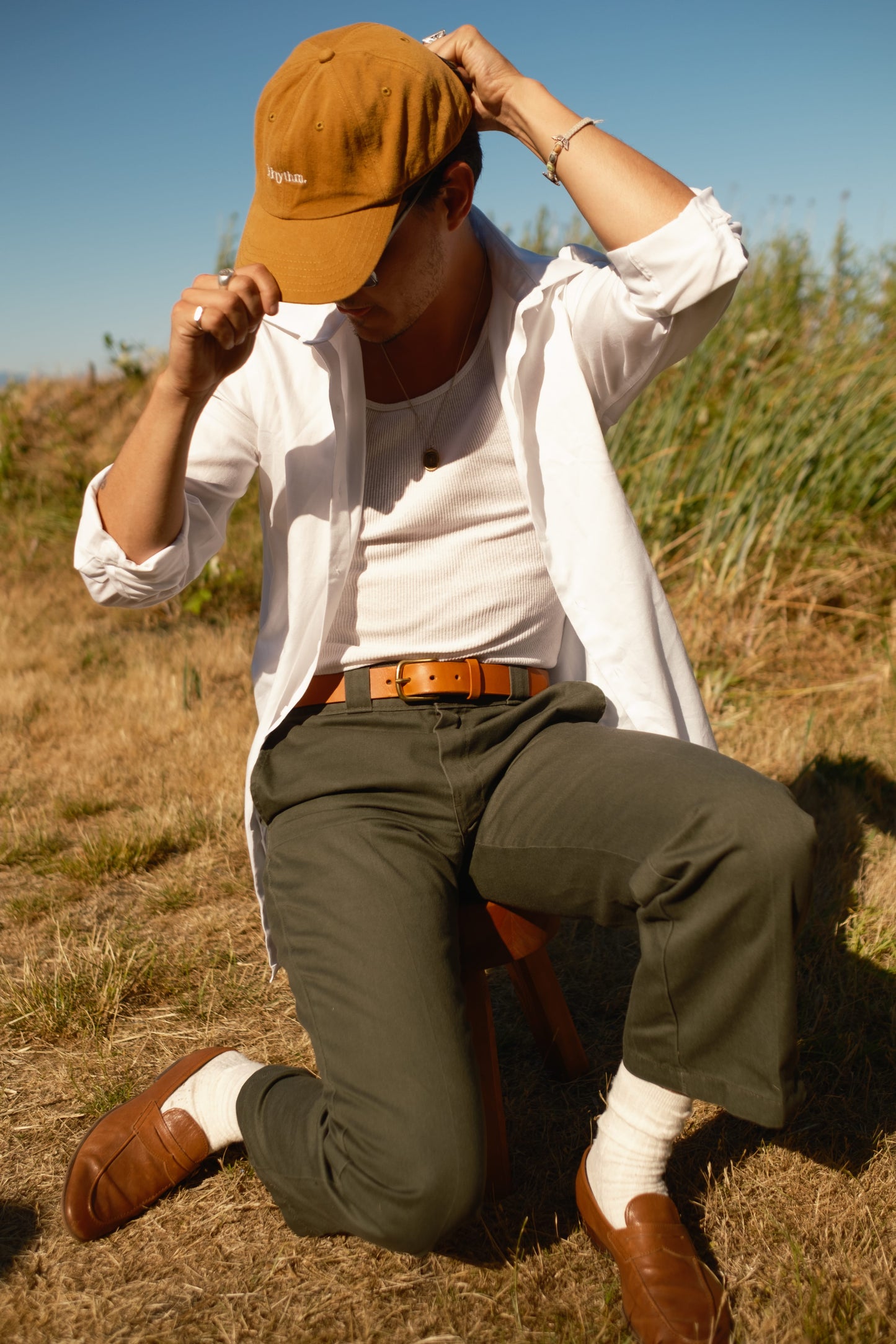 Person wearing a white shirt, green pants, and brown cap sitting in a field.