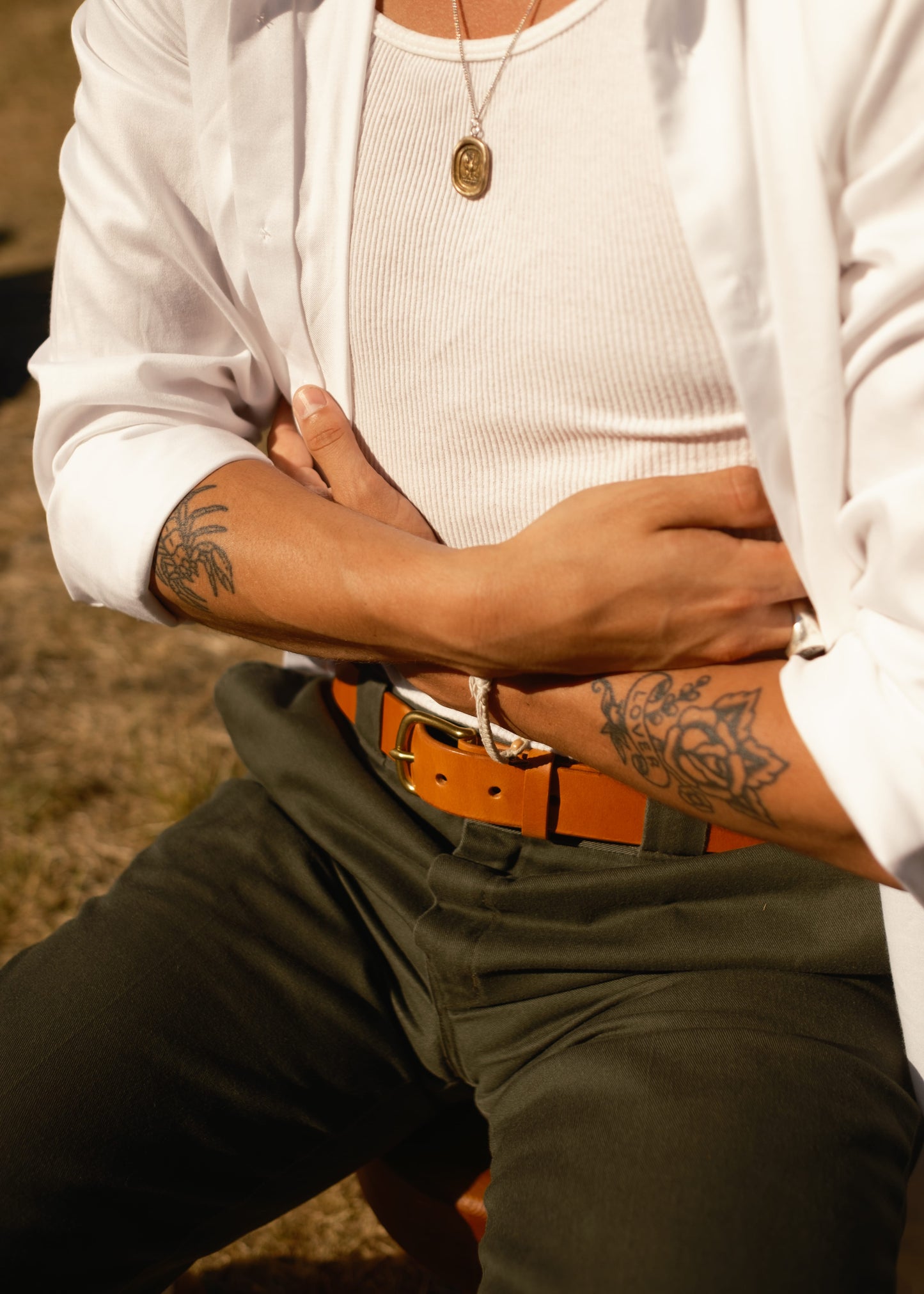 Person wearing a white shirt, beige pants, and an orange belt with tattoos on arms.