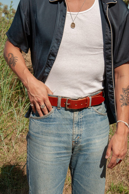 Person wearing a black jacket, white shirt, blue jeans, and red belt outdoors.