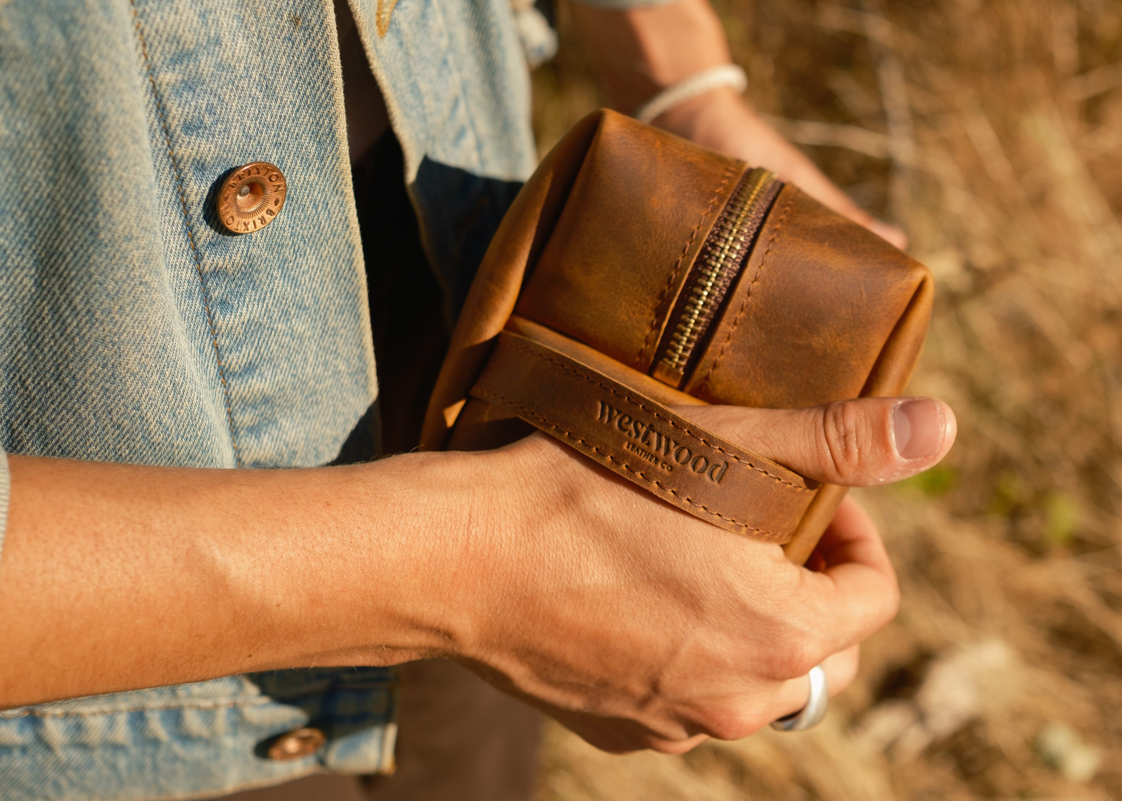 Person holding a brown leather bag with 'Westwood' branding outdoors.