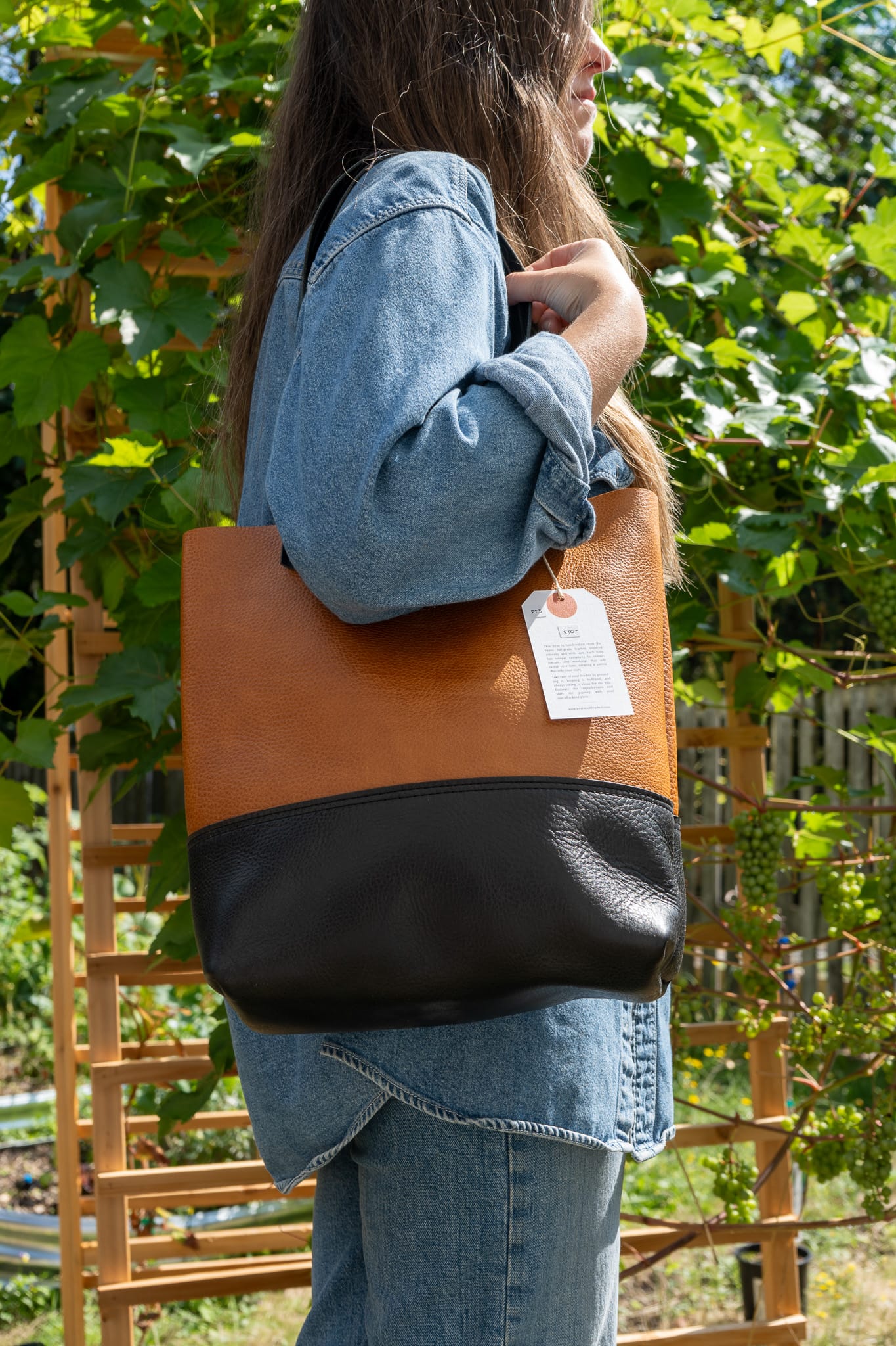 Person holding a brown and black tote bag with a visible tag, standing outdoors.