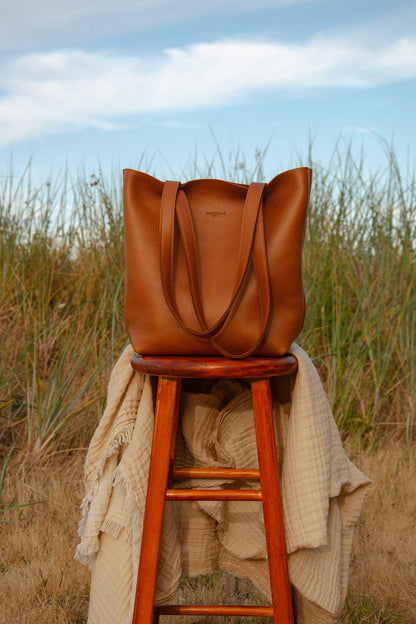 Tan tote bag on a wooden stool with grass and blue sky in the background
