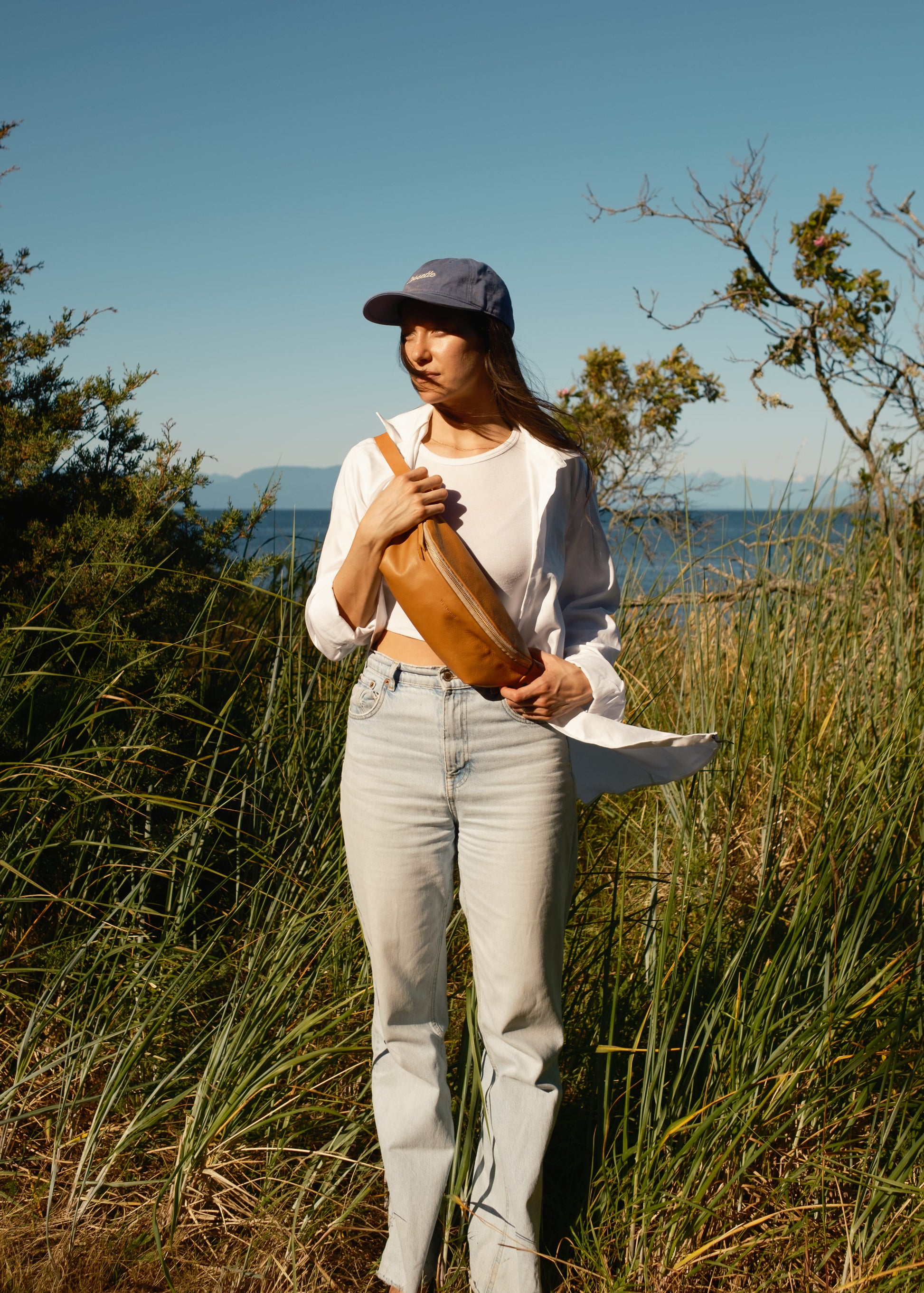 Woman holding a leather bag in a natural setting with trees and water in the background