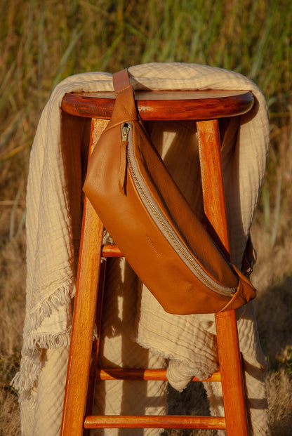 Brown leather bag on a wooden stool with a textured blanket in a natural setting