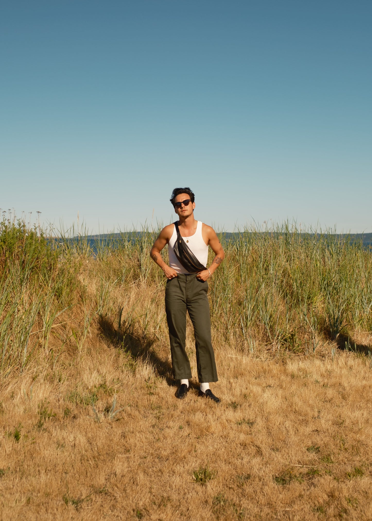 Person standing in a field with tall grass and a clear blue sky