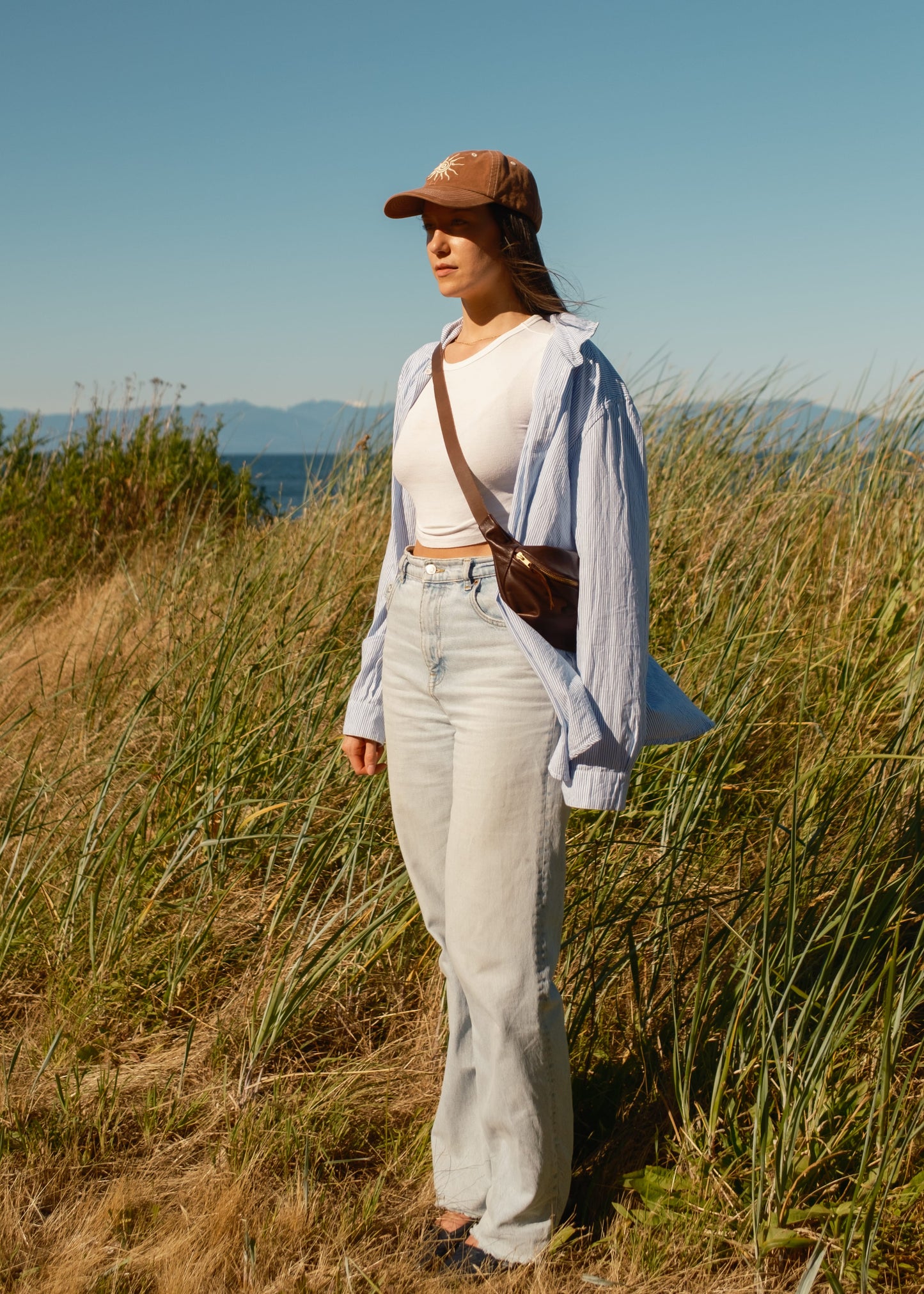 Person standing in a grassy field wearing a cap, light shirt, and jeans.