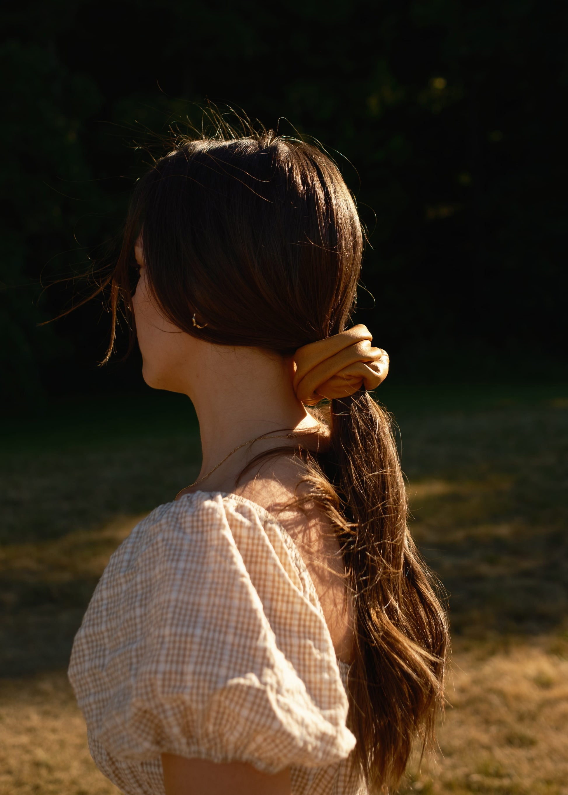 Person with long hair tied back in a ponytail, standing outdoors with a blurred natural background