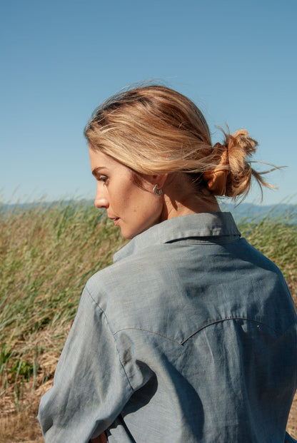 Woman with a bun in her hair standing in a field with a clear blue sky.