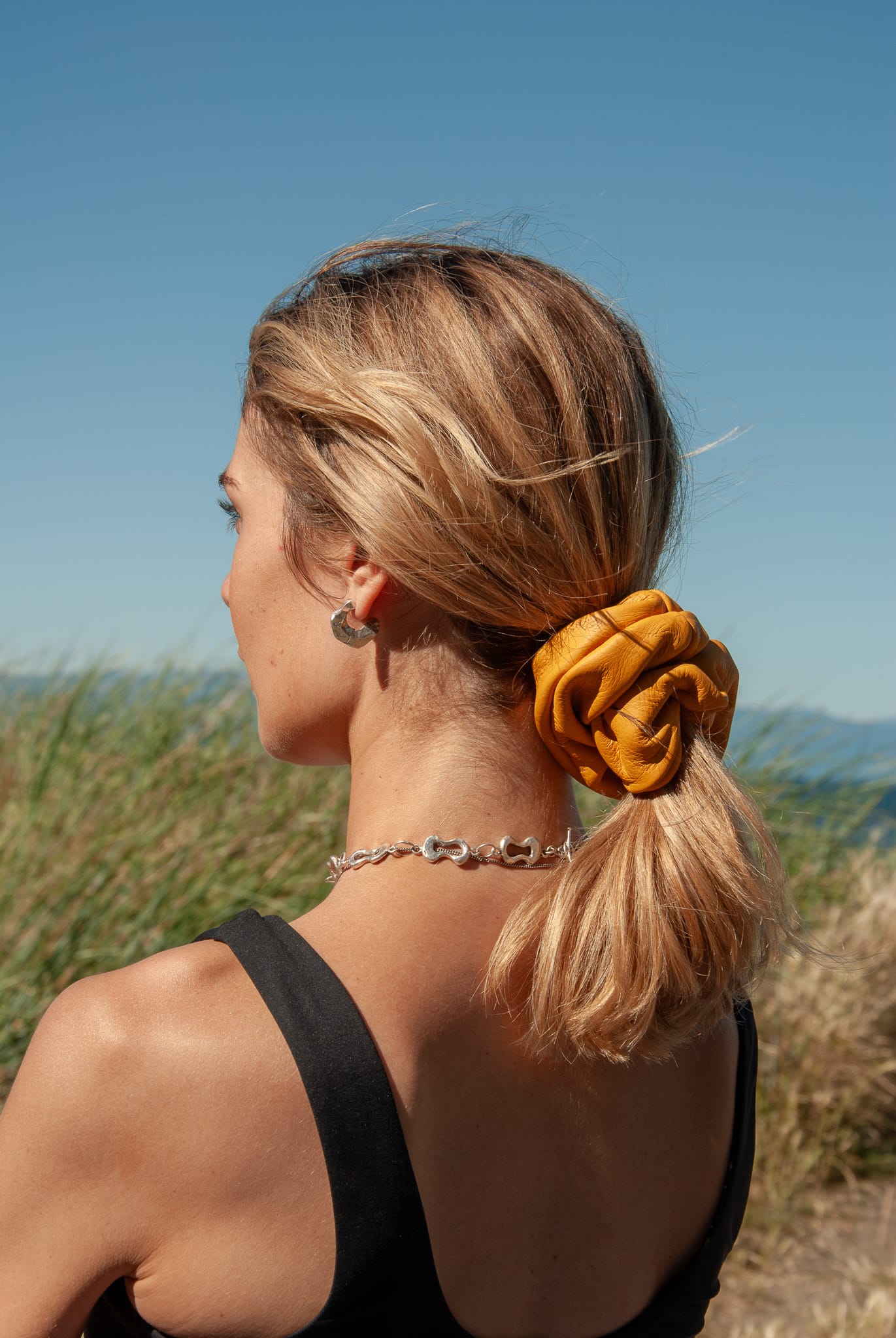 Woman with a yellow scrunchie in her hair against a blue sky and grassy background