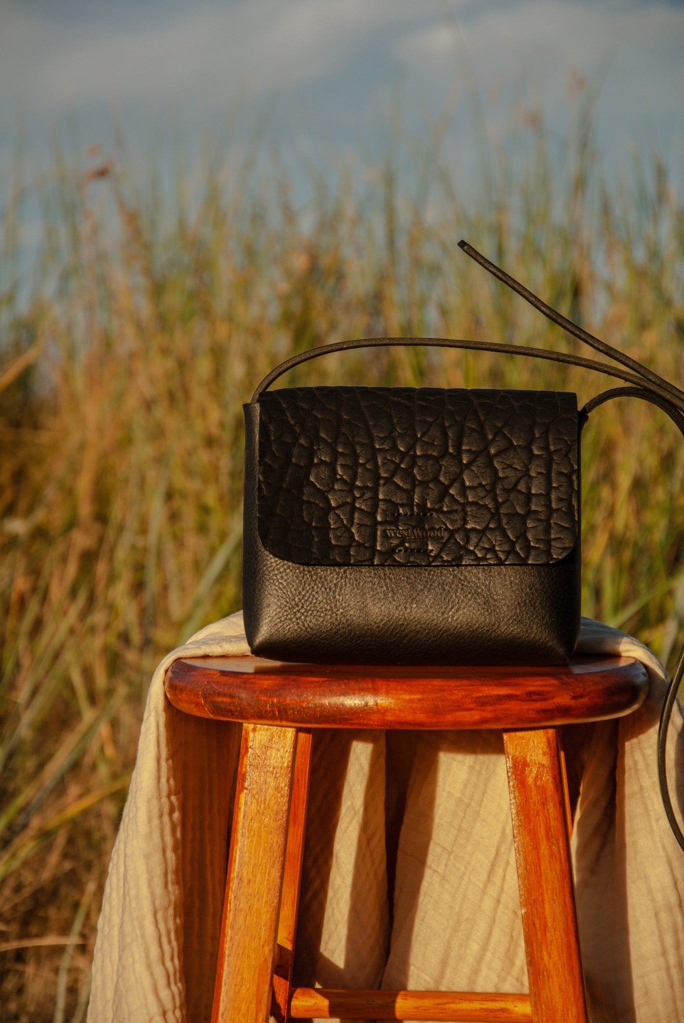 Black textured handbag on a wooden stool with a natural background