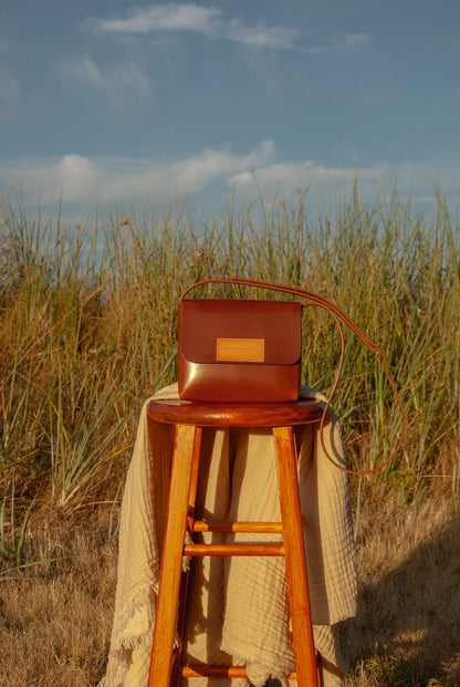 Brown leather bag on a wooden stool in a field with a blue sky.