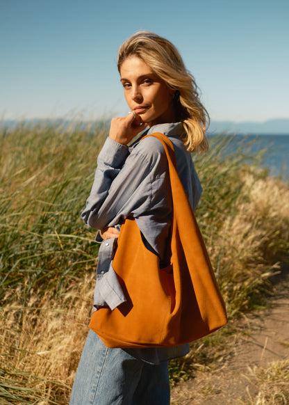 Woman holding a honey brown bag in a grassy outdoor setting