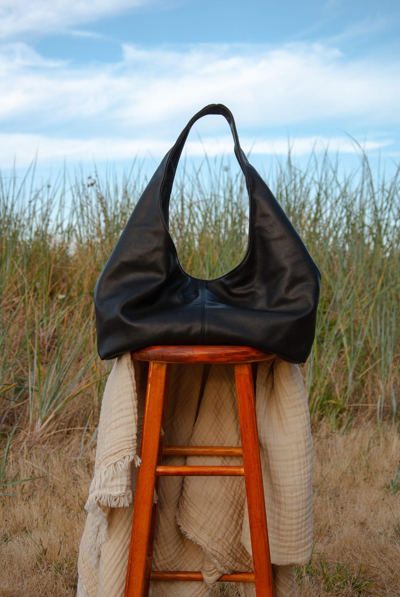 Black leather handbag on a wooden stool with a natural background