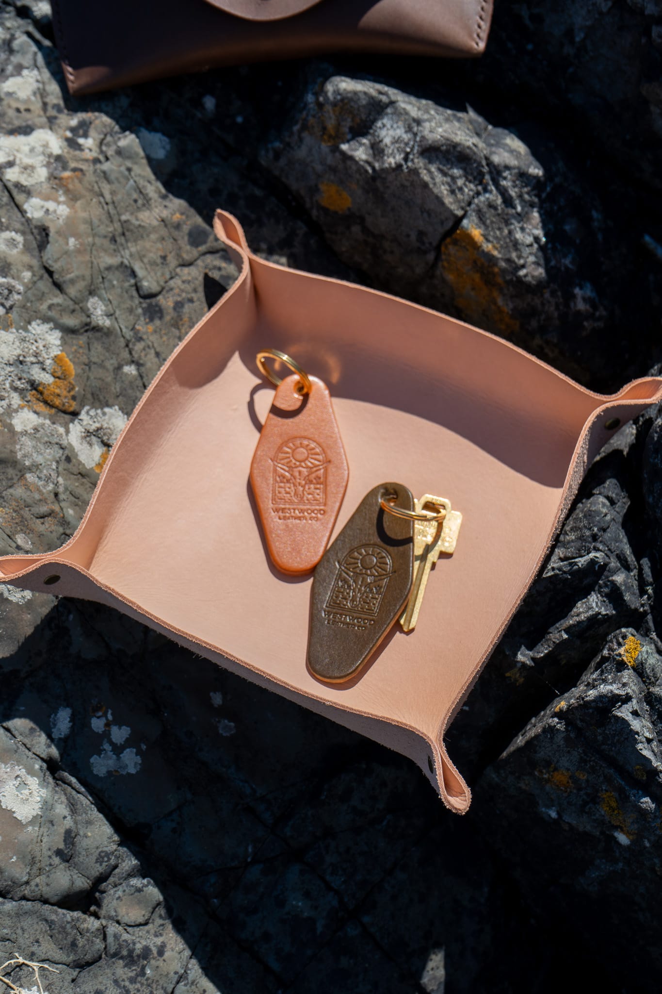 Pink leather tray with keys on a rocky surface