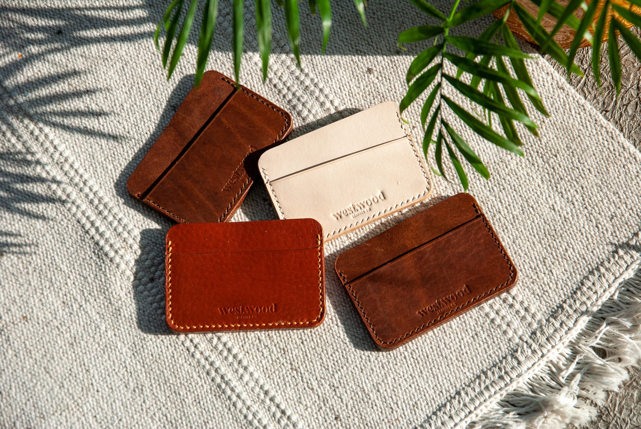 four leather cardholders on a white woven rug with the shadow of a palm leaf overhead