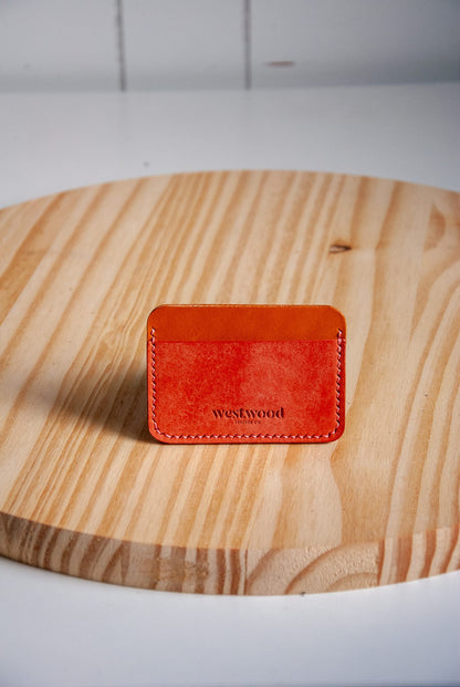Pink leather cardholder with 'westwood' branding on a wooden surface