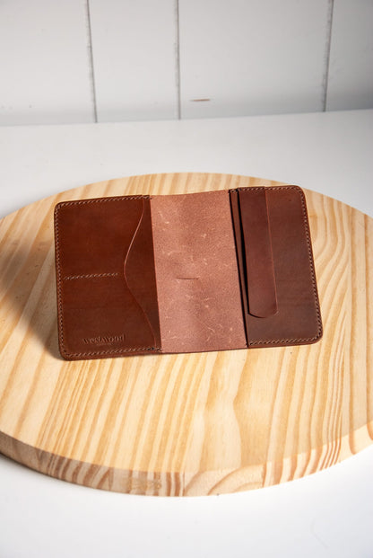 Brown leather wallet on a wooden surface with a white cushioned background