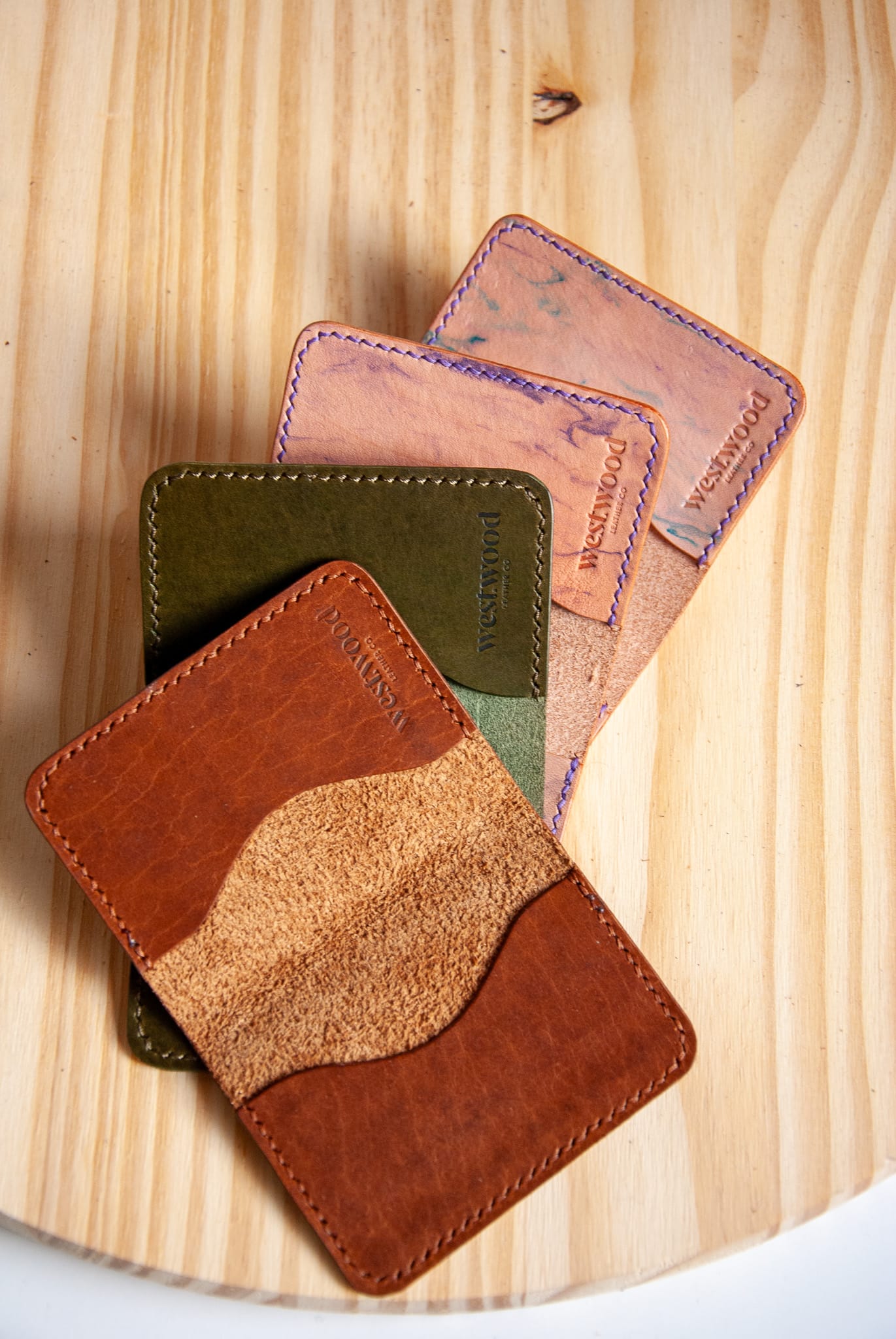 Four leather card holders in different colors on a wooden surface
